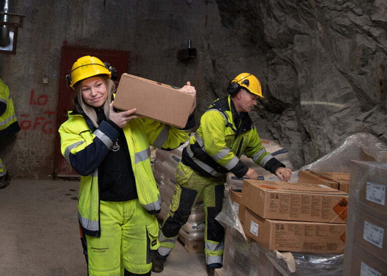 Person i skyddskläder och hjälm bär låda i gruva