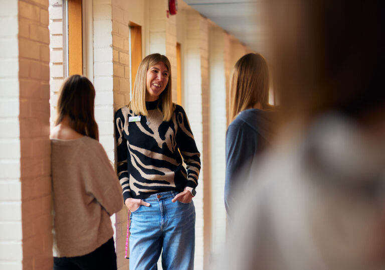 Kvinna pratar med två högstadietjejer i skolkorridor