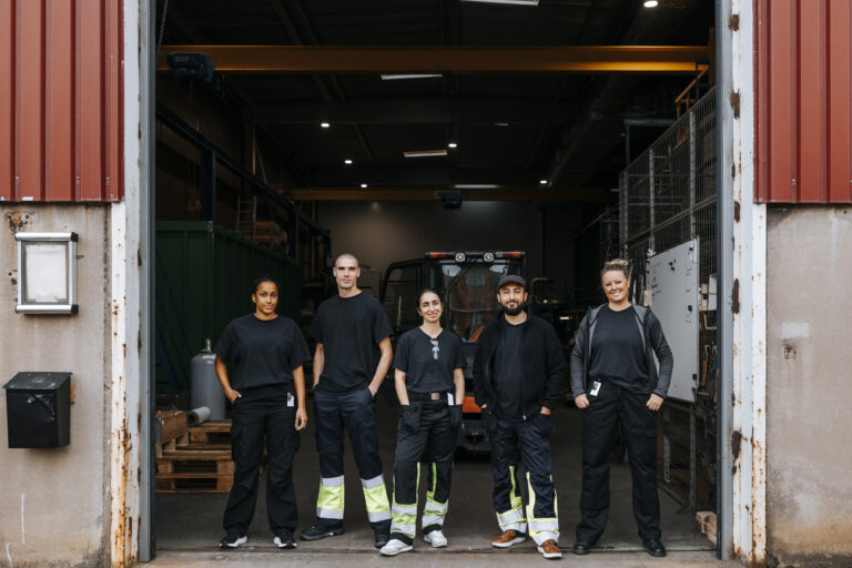 Fem personer står framför en lagerbyggnad.