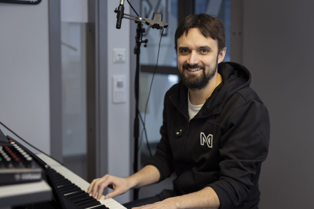 En man sitter vid ett keyboard framför en mikrofon.