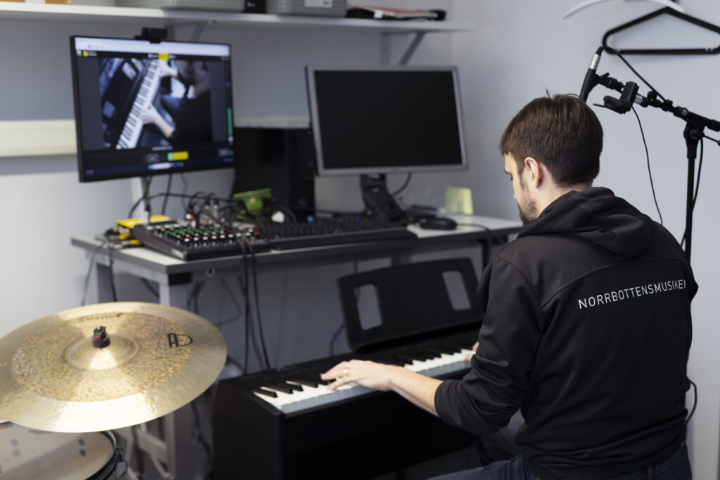 En man sitter vid ett keyboard framför en mikrofon.